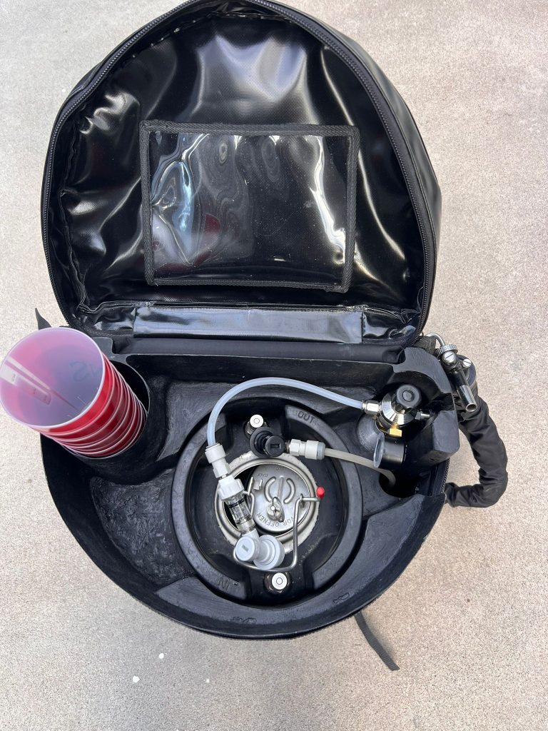 Internal view of the DraftGo mobile beverage dispenser backpack showing the CO₂ bottle, pressure regulator, 11L tank, tubing and cup holder.